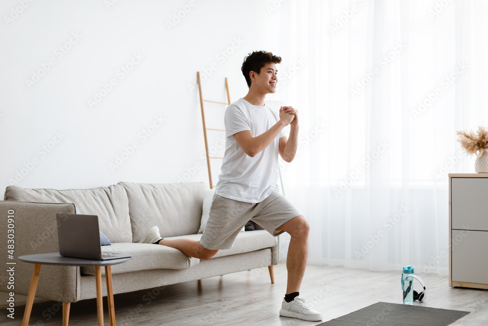 Asian guy doing split squats in front of laptop Asian guy doing split squats in front of laptop
