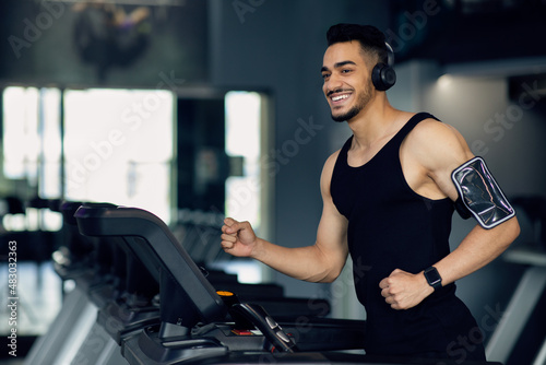 Fotografie, Tablou Handsome Muscular Arab Man In Wireless Headphones Jogging On Treadmill At Gym