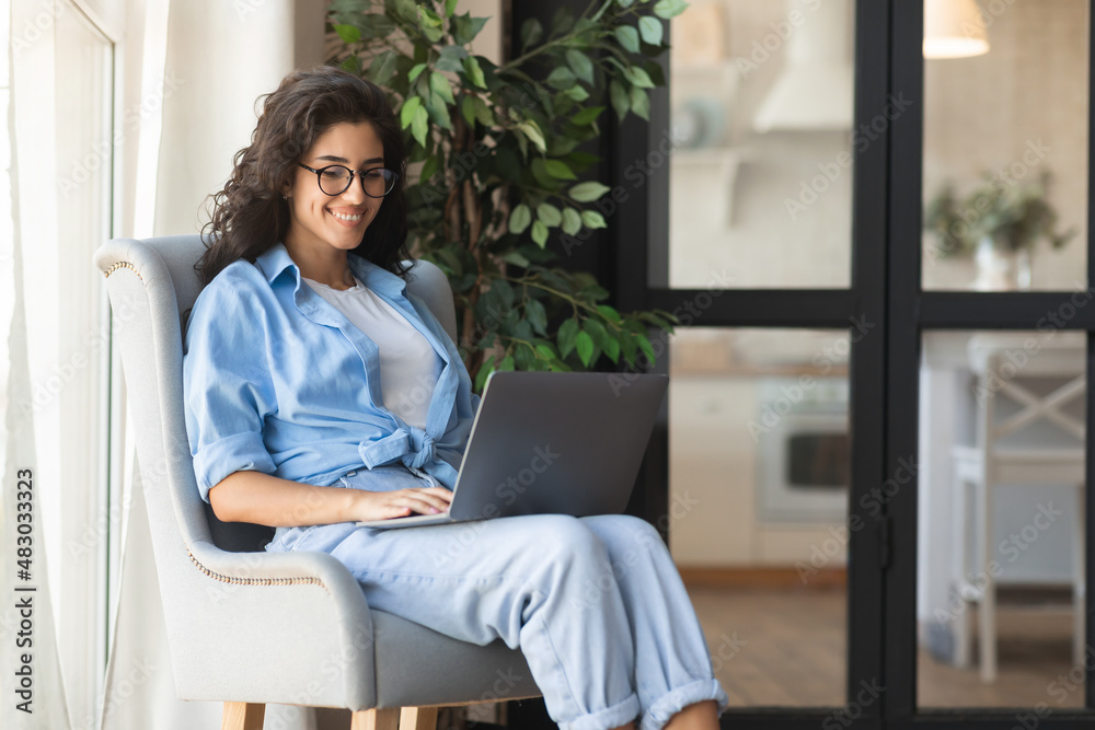 Happy young female freelancer having online business meeting on laptop, sitting in comfy armchair at home, copy space Happy young female freelancer having online business meeting on laptop, sitting in comfy armchair at home, copy space