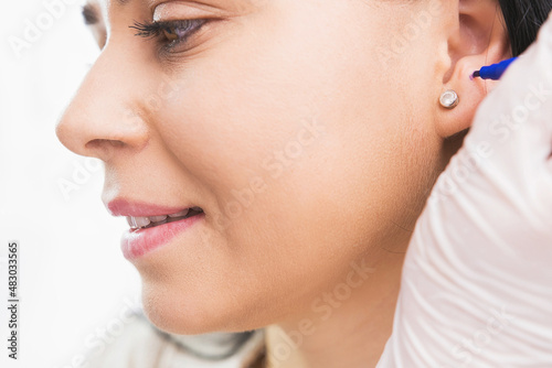 Quadro em tela Close up photo of a side of the woman face, specialist female in gloves making dot with medical marker on a woman ear to pierce it in the cosmetologist cabinet