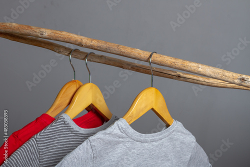 Clothes made of natural cotton hang on wooden hangers on a crossbar made of a stick. The concept of eco-clothing in gray and red