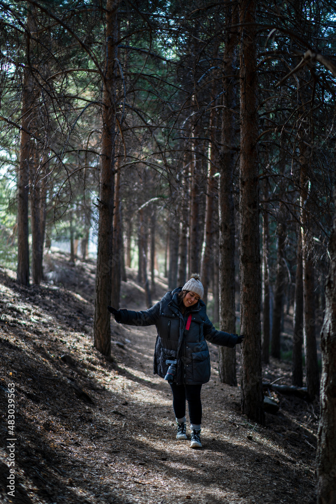 Chica joven guapa en un bosque de arboles altos con cámara de foto colgada al cuello Chica joven guapa en un bosque de arboles altos con cámara de foto colgada al cuello