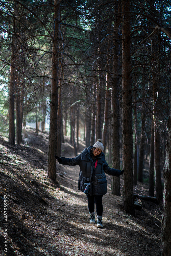 Chica joven guapa en un bosque de arboles altos con cámara de foto colgada al cuello