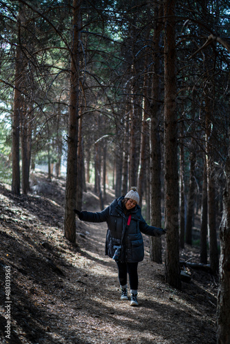 Chica joven guapa en un bosque de arboles altos con cámara de foto colgada al cuello