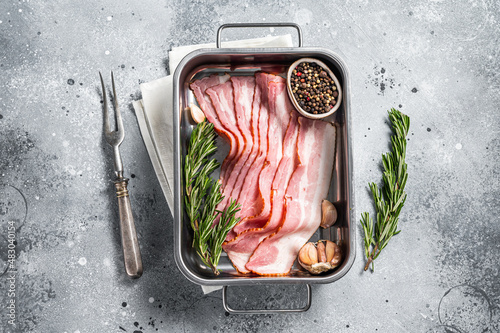 Raw smoked bacon slices with rosemary and garlic. Gray background. Top view