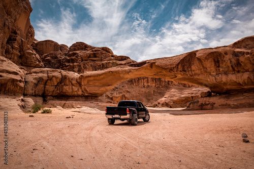A car in view through a rock arch in the desert of Wadi Rum