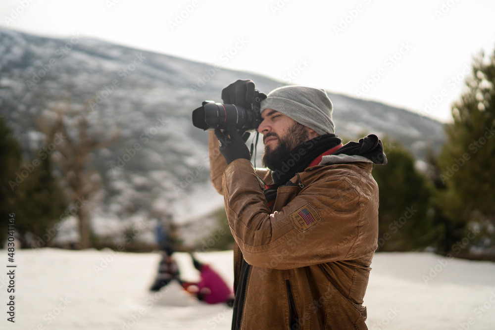 Chico con barba en la nieve con camara de fotos con ropa marron