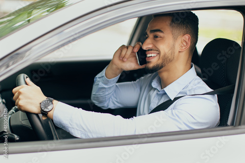 Cheerful arab man talking on cellphone while driving car © Prostock-studio