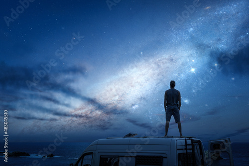 Leinwand Poster Starry sky above a man standing on the roof of his camper van