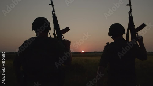 Two military people in special equipment walking across field holding rifles.