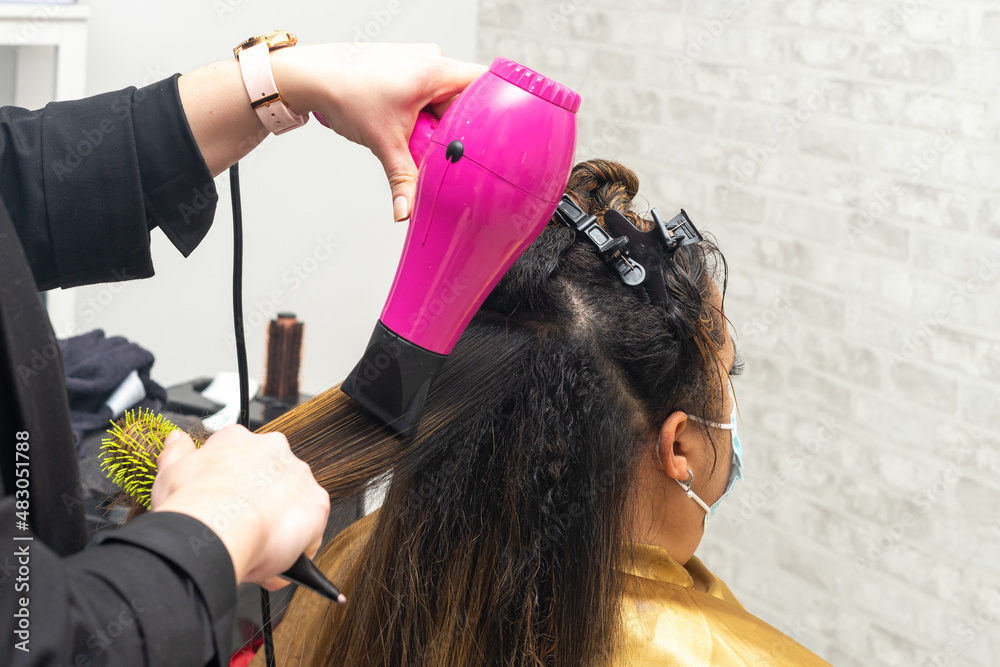 Fototapeta premium Hairdresser drying the hair of a client with damaged hair in a beauty salon using a hairdryer and a round brush. Close up. Copy Space. High quality photo