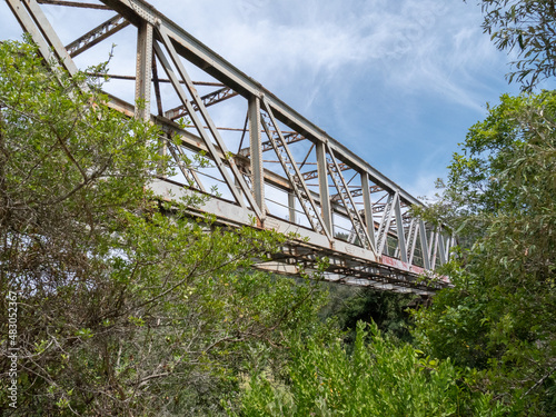 Side profile of a stainless steel railway bridge amongst green bushes