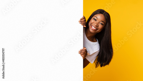 Black woman peeking out blank white advertising billboard at studio