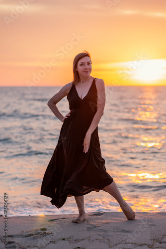 Beautiful woman stands in a dress near the sea at sunset
