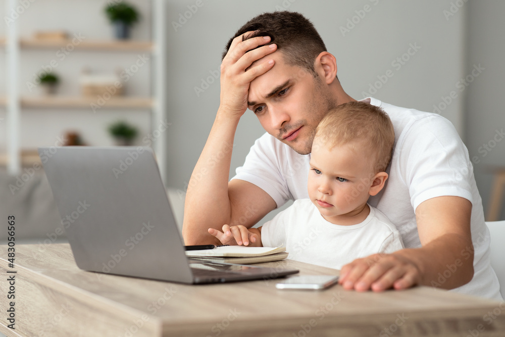 Stressed father with infant baby on hands working on laptop at home Stressed father with infant baby on hands working on laptop at home