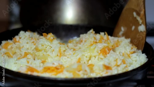 Rice porridge with fried carrots and onions is mixed with a wooden spoon closeup