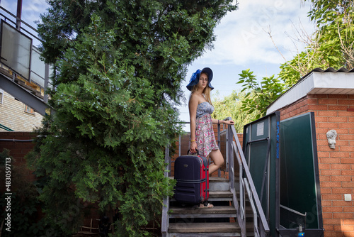 a young girl in a sundress with a suitcase is standing on the stairs