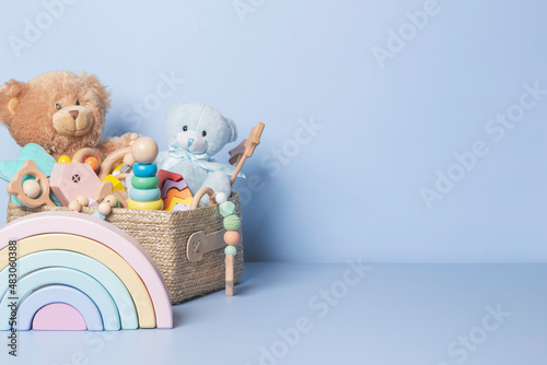 Toy box full of baby kid toys. Container with teddy bear, wooden rattles, stacking pyramid and wood blocks on light blue background. Cute toys collection for small children. Donatation. Front view photo