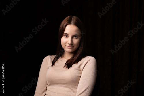 Portrait of a young woman on a dark background. The girl in the brown sweater. Friendly face looking at the camera.