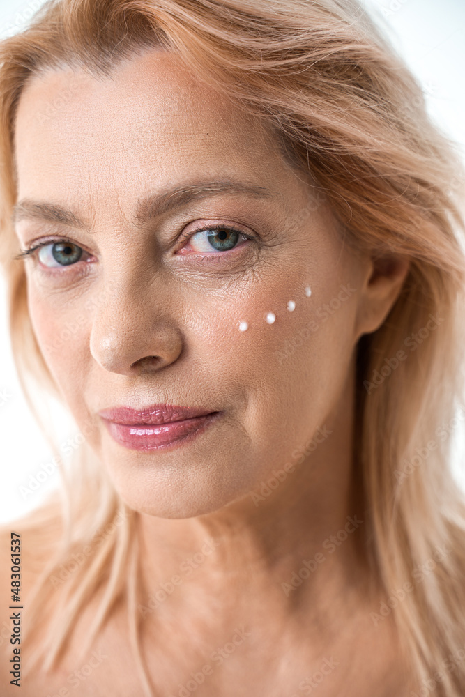 Obraz premium Serious caucasian woman with applying points of facial moisturizer while looking at camera