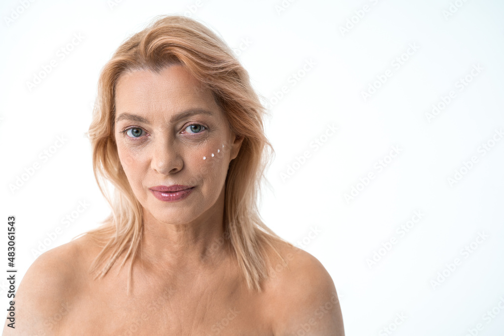 Mature woman with points of moisturizer cream on her face looking at the camera with smile Mature woman with points of moisturizer cream on her face looking at the camera with smile