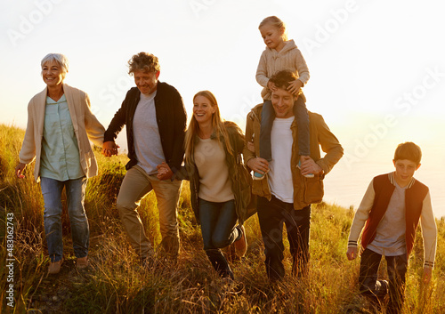 Together every step of the way. A multi-generational family walking up a grassy hill together at sunset.