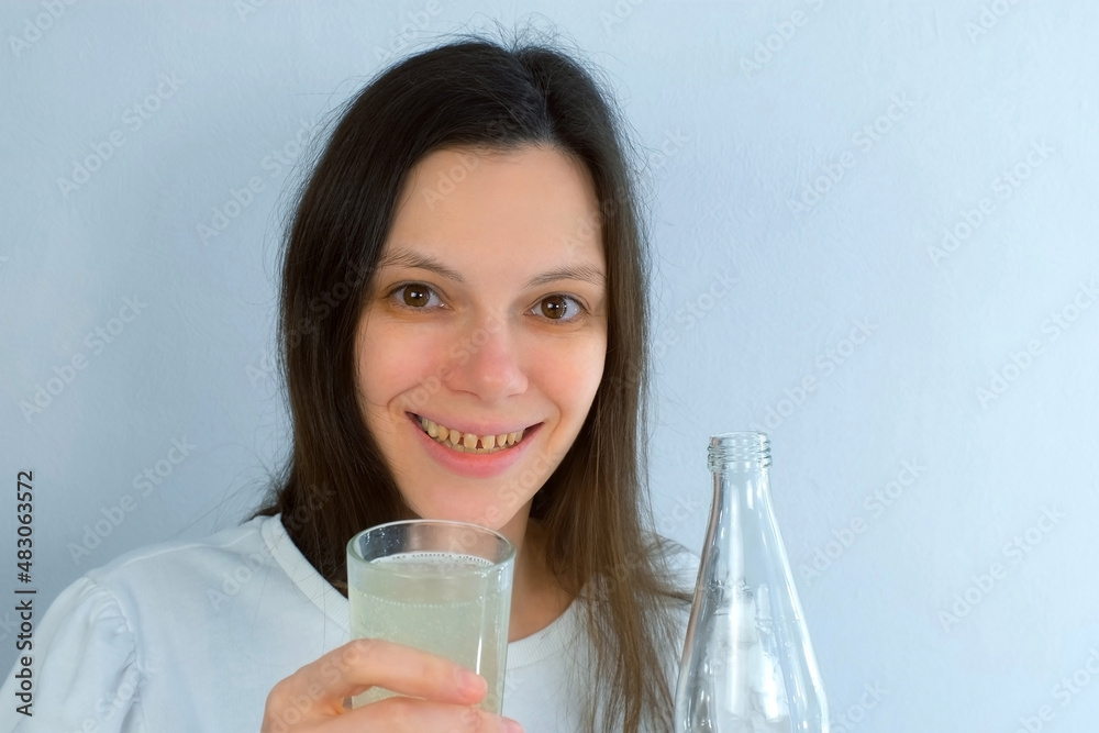 Portrait of woman with yellow bad teeth pouring lemonade in glass and smiling. Bad habits for dental health, destructive effect when using sugar and carbonated drinks. Terrible smile of young woman. Portrait of woman with yellow bad teeth pouring lemonade in glass and smiling. Bad habits for dental health, destructive effect when using sugar and carbonated drinks. Terrible smile of young woman.