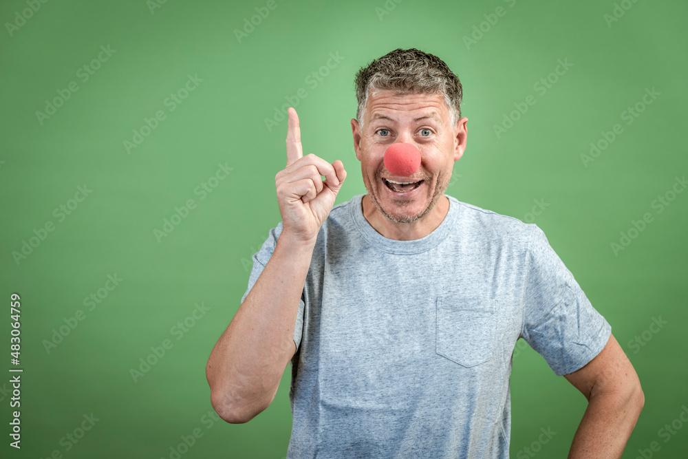 man with red clown nose and grey shirt in front of green background man with red clown nose and grey shirt in front of green background