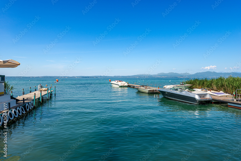 Small port on the coast of Lake Garda (Lago di Garda) with speedboats between the village of Lazise and Bardolino, tourist resorts in Verona province, Veneto, Italy, Europe. Lombardy on the horizon.