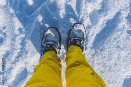 A first-person POV shot of a woman's legs in ski pants and snowshoes standing during a hike in the French Alps on a cold winter day (L'Enclus, Devoluy, Hautes-Alpes)