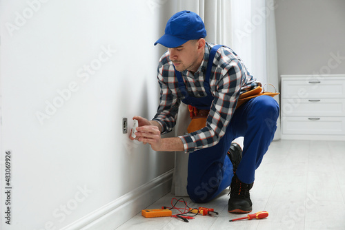 Professional male electrician repairing power socket in room