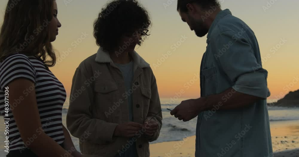 Happy friends standing on beach playing with sparklers and having fun