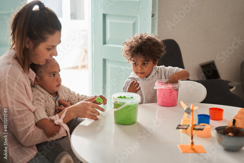 Child boys and mother playing with building sand at home while sitting at the table at the kitchen