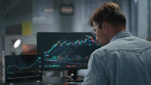 Rear view of trader working with stock market on laptop late in office