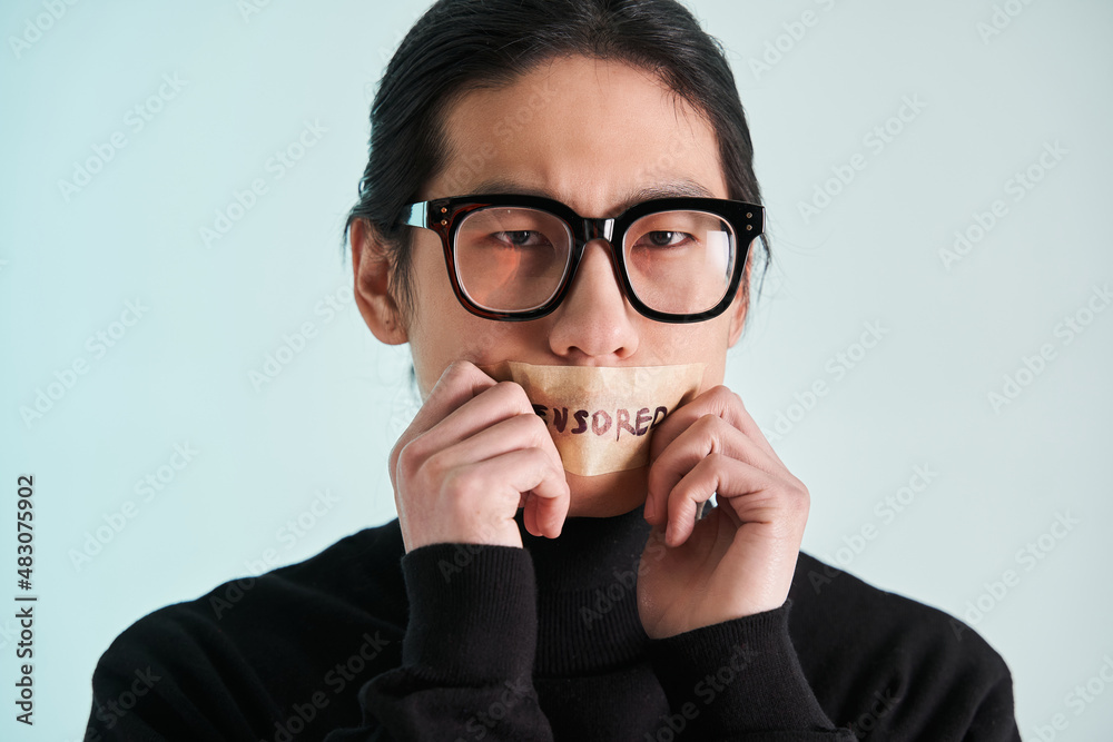 Asian man with censored sign on his lips holding ands near his face Asian man with censored sign on his lips holding ands near his face