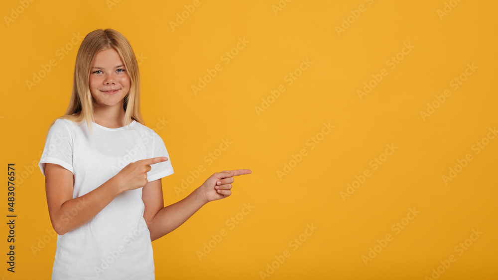 Cheerful european teen girl student in white t-shirt pointing fingers at empty space, isolated on yellow background Cheerful european teen girl student in white t-shirt pointing fingers at empty space, isolated on yellow background