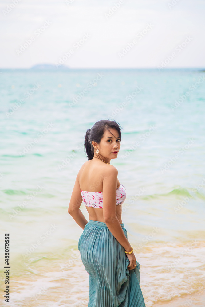 Backside An Asian woman in bikini with dress standing in front of the sea and looking at a camera with sea and sky background. Backside An Asian woman in bikini with dress standing in front of the sea and looking at a camera with sea and sky background.