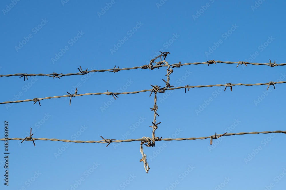 Close-up of part of prison fence with barbed wire against blue sky Close-up of part of prison fence with barbed wire against blue sky