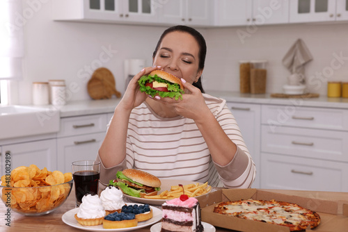 Overweight woman eating burger in kitchen at home photo
