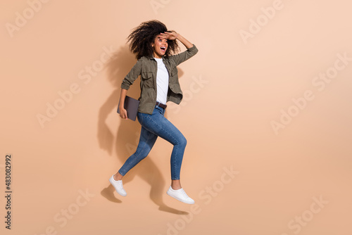 Full length body size view of pretty cheerful girl jumping carrying laptop finding way isolated over beige pastel color background