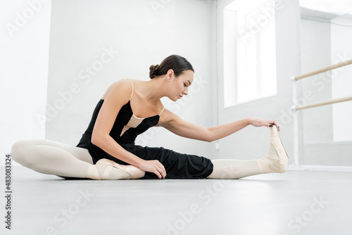 pretty brunette ballerina stretching while sitting on floor in studio