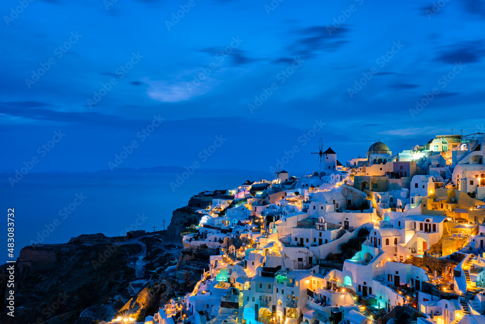 Famous greek iconic picturesque tourist destination Oia village with traditional white houses and windmills in Santorini island in the evening blue hour, Greece