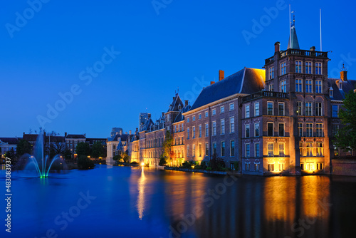 View of the Binnenhof House of Parliament and the Hofvijver lake with downtown skyscrapers in background illuminated in the evening. The Hague, Netherlands