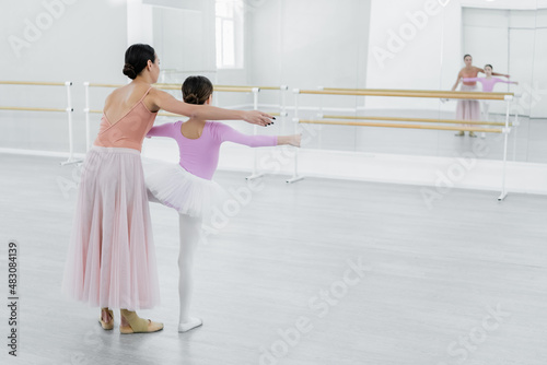 back view of girl training in ballet school near mirrors and young dance teacher photo