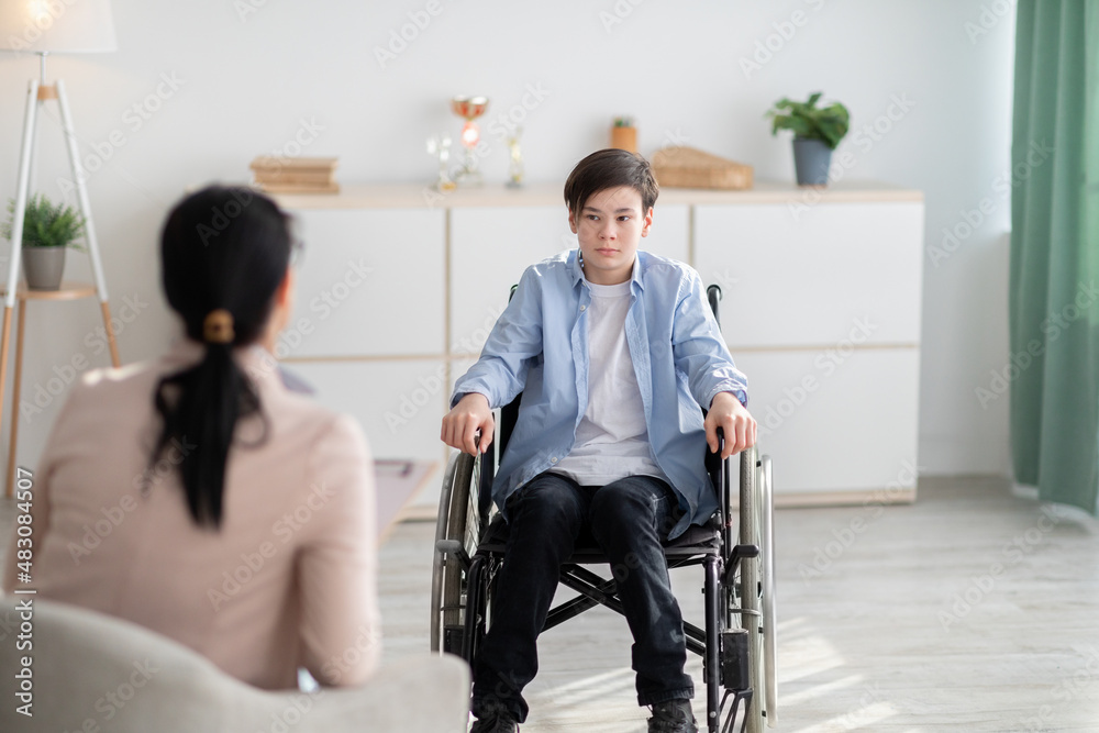 Psychological help service. Disabled teen boy in wheelchair having psychotherapy session with counselor at clinic Psychological help service. Disabled teen boy in wheelchair having psychotherapy session with counselor at clinic