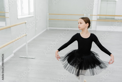 Fototapeta girl in black ballet costume making curtsy while training in dancing hall
