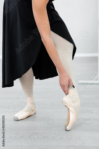 cropped view of ballerina in black dress and pointe shoes rehearsing in studio