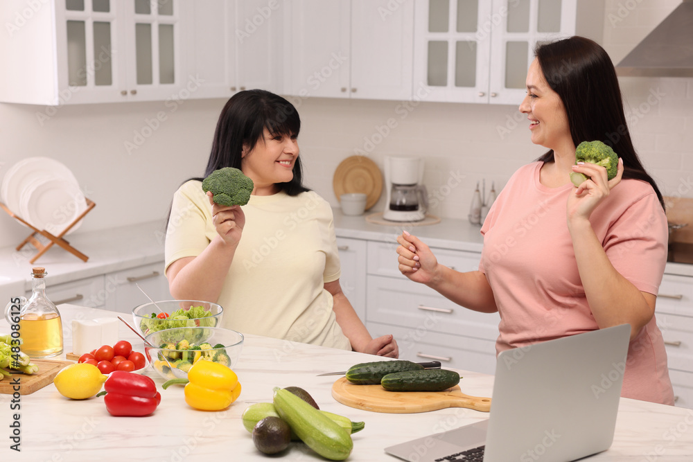 Happy overweight women having fun while cooking together in kitchen
