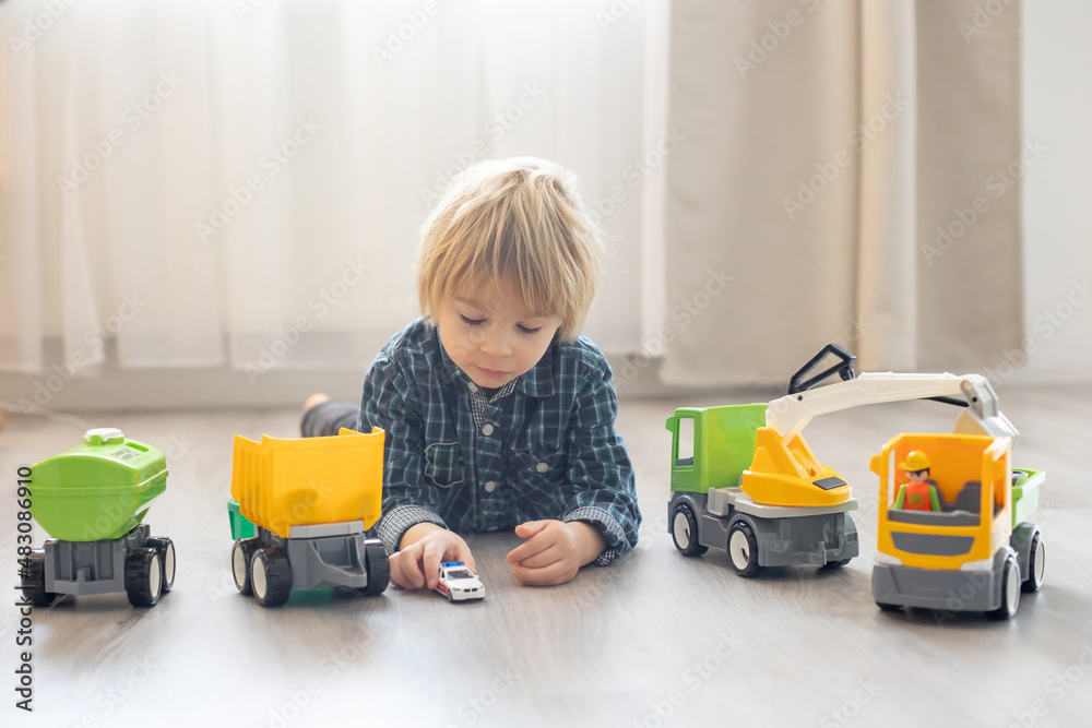 Cute toddler blond child in front of a teepee, playing with big cars on the floor Cute toddler blond child in front of a teepee, playing with big cars on the floor
