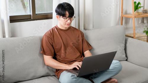 Technology Concept The male who is wearing casual clothes sitting on the sofa, resting his notebook on his lap and doing his work